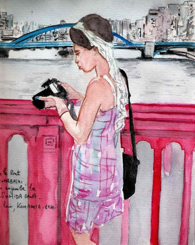 Femme tenant un appareil photo, devant un pont au bord de l'eau. 