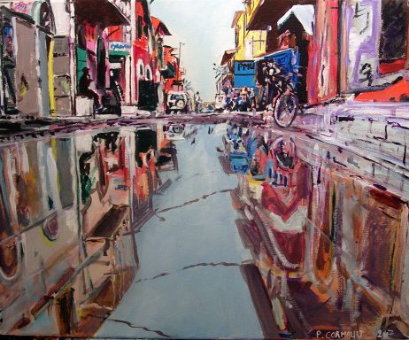 Rue animée avec des bâtiments colorés et des reflets dans une flaque d'eau.