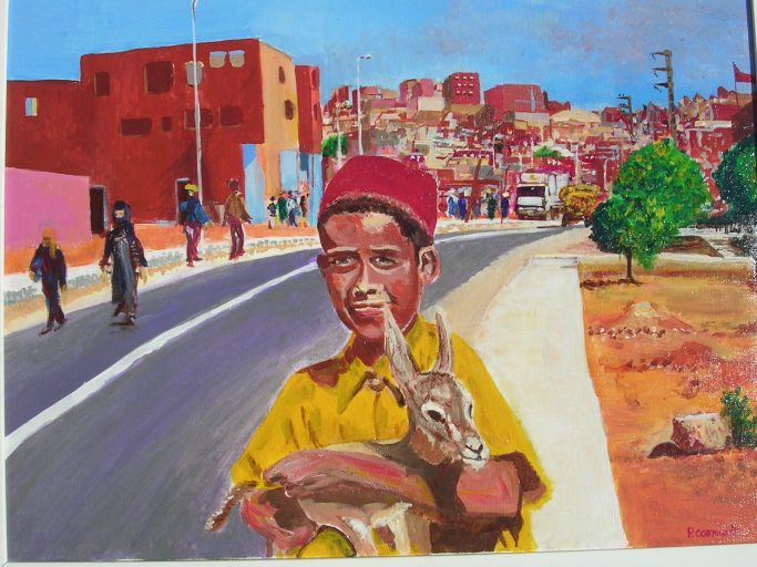 Un jeune garçon en vêtement traditionnel tient un chevreau sur une route entourée de bâtiments.